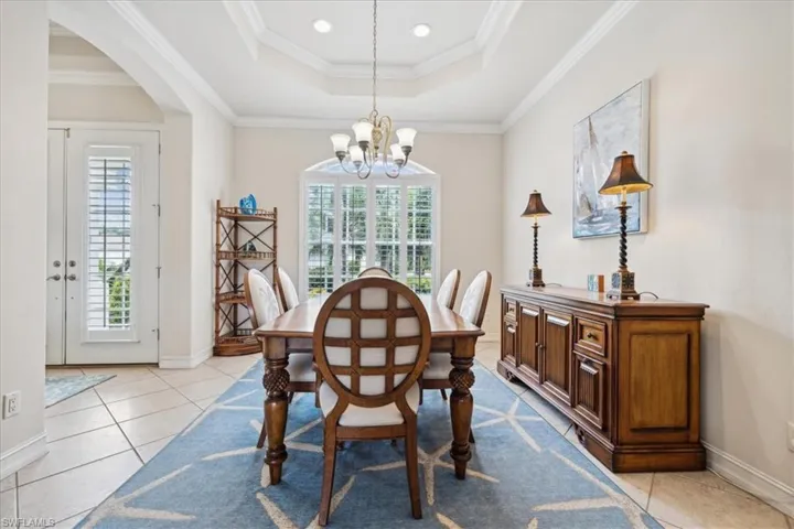 Tiled dining room featuring plenty of natural light, a raised ceiling, ornamental molding, and a notable chandelier