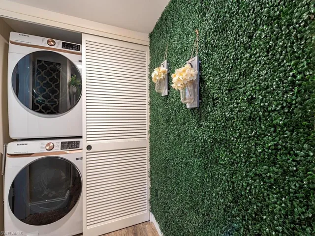 Clothes washing area with stacked washer and clothes dryer, wood finished floors, and laundry area