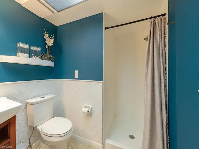Full bath with tile walls, toilet, a shower stall, wainscoting, and vanity