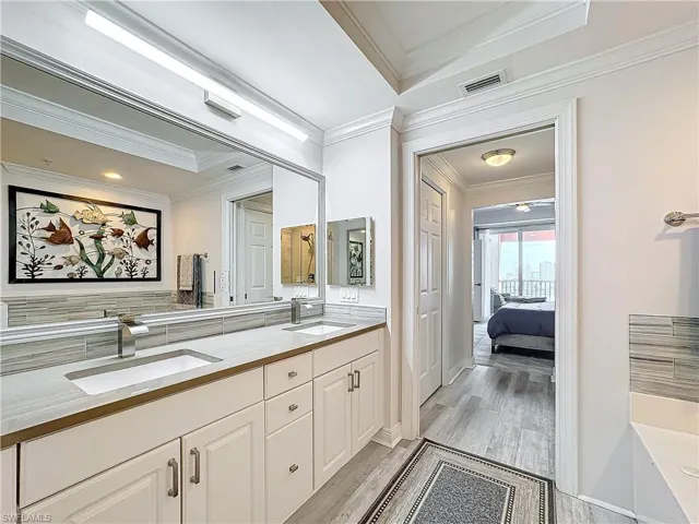 Bathroom featuring dual vanity, decorative backsplash, wood-type flooring, and ornamental molding