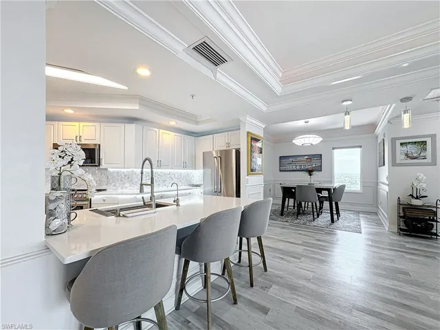 Kitchen with tasteful backsplash, hanging light fixtures, ornamental molding, light hardwood / wood-style floors, and appliances with stainless steel finishes