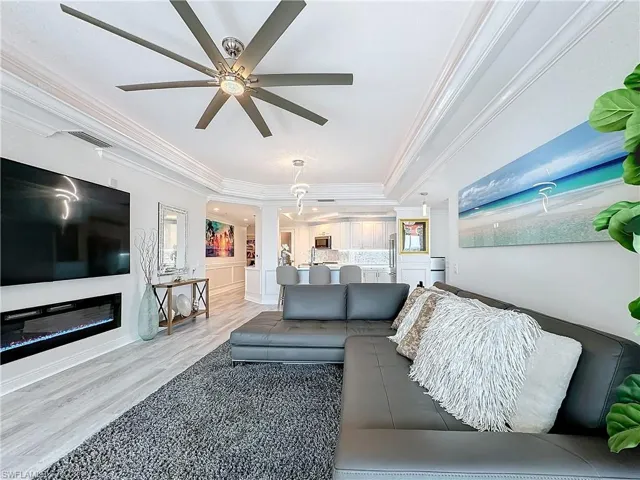 Living room with ceiling fan, crown molding, a tray ceiling, and light hardwood / wood-style floors
