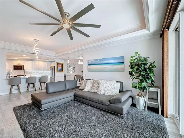 Living room featuring ornamental molding, light hardwood / wood-style flooring, ceiling fan, and a tray ceiling