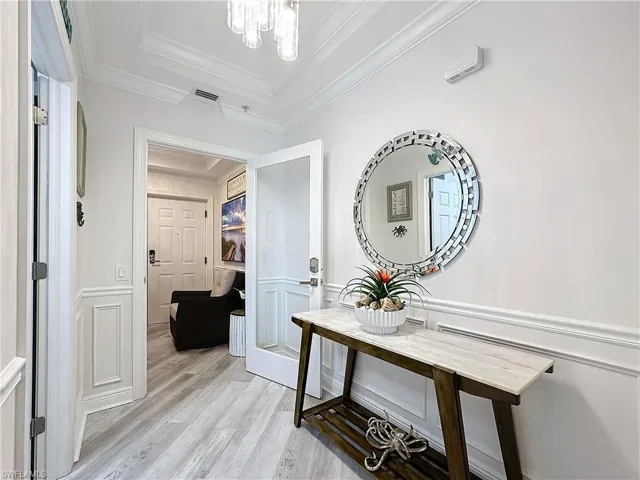 Hallway featuring light hardwood / wood-style flooring, a raised ceiling, ornamental molding, and a notable chandelier