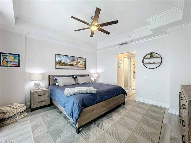 Bedroom featuring ornamental molding, light hardwood / wood-style flooring, ceiling fan, and a tray ceiling
