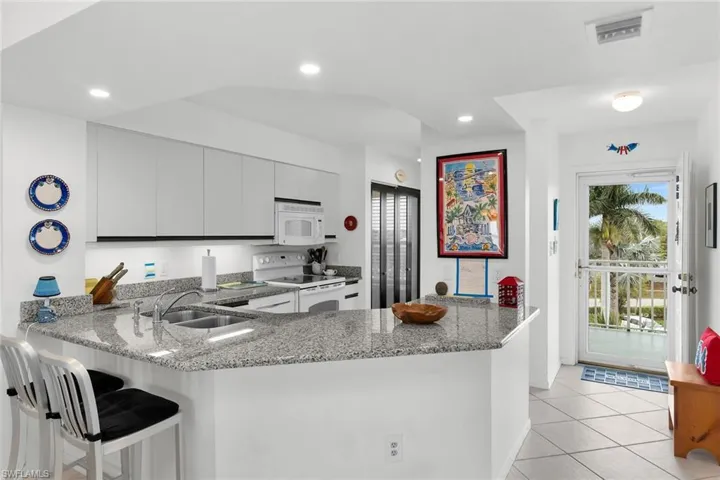 Kitchen with a peninsula, white appliances, light stone countertops, a breakfast bar, and light tile patterned floors