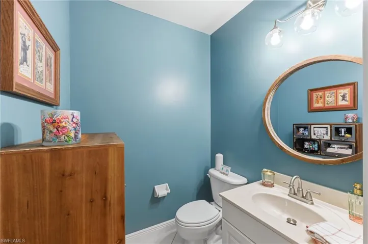 Powder room featuring a single vanity with a white countertop and base, a round framed mirror, a toilet, and a wall-mounted light fixture
