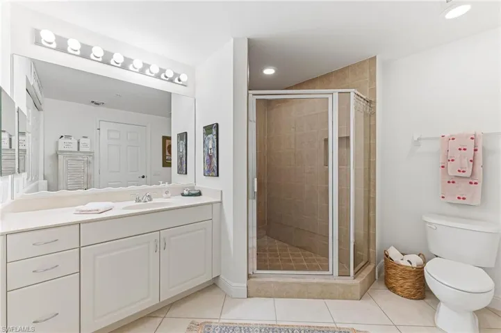 Bathroom featuring a vanity with an integrated sink, a large wall-mounted mirror with overhead vanity lighting, a glass-enclosed shower with tiled walls and floor, and tile flooring throughout
