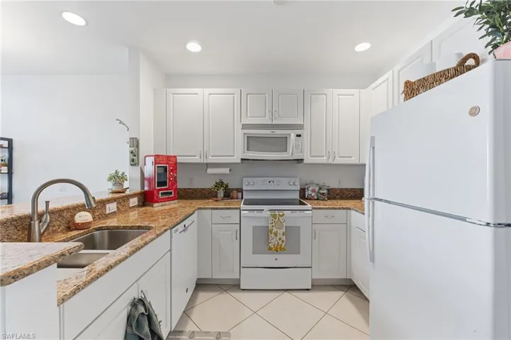 Well-appointed kitchen featuring white cabinetry, light-colored stone countertops, and white appliances
