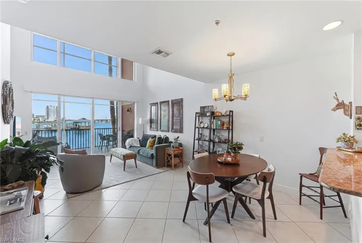 Open-concept living and dining area featuring high ceilings, upper transom windows, and a water-facing balcony with sliding glass doors
