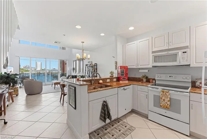 Open-concept kitchen featuring white cabinetry, a built-in microwave, and stone-finish countertops