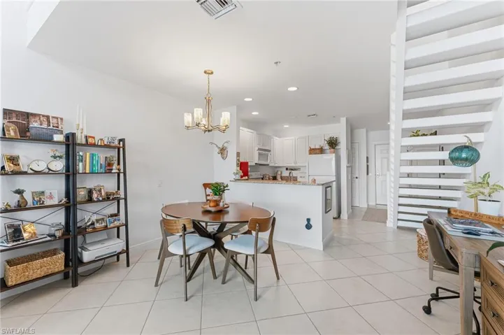 Open-concept living area featuring a kitchen with white cabinetry and light-toned countertops, a dining space with an overhead chandelier, and light-colored tile flooring throughout