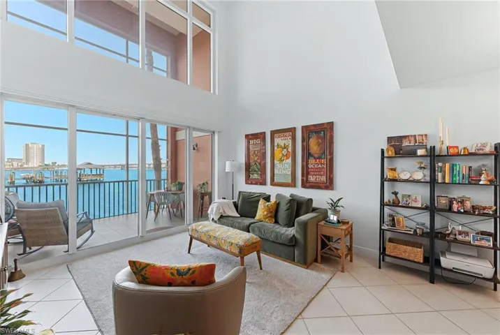 Living area featuring high ceilings, a wall of sliding glass doors, upper transom windows, a balcony, and waterside views