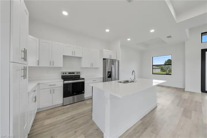 Kitchen featuring appliances with stainless steel finishes, recessed lighting, white cabinetry, a kitchen island with sink, and light countertops