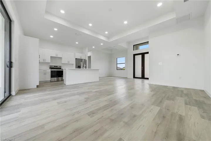Unfurnished living room with a raised ceiling, recessed lighting, light wood-style flooring, and a high ceiling