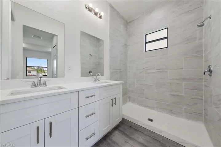 Full bathroom featuring double vanity, a tile shower, and wood finished floors