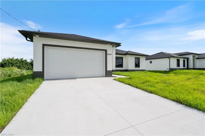 View of front of property with stucco siding, concrete driveway, a front lawn, and a garage