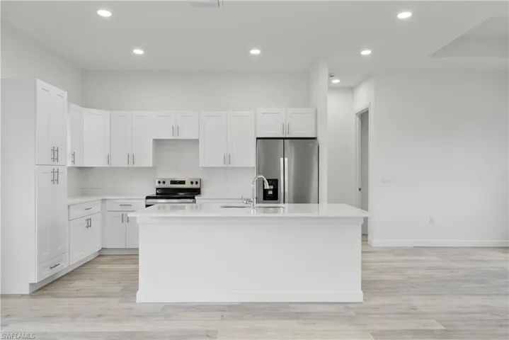 Kitchen with stainless steel appliances, recessed lighting, an island with sink, light countertops, and white cabinetry