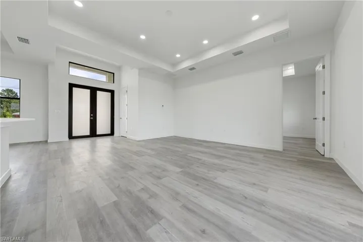 Unfurnished living room featuring a tray ceiling, recessed lighting, light wood finished floors, and french doors