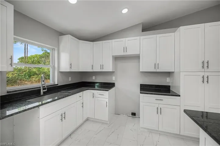 Kitchen with dark stone counters, light marble finish floors, white cabinetry, vaulted ceiling, and recessed lighting