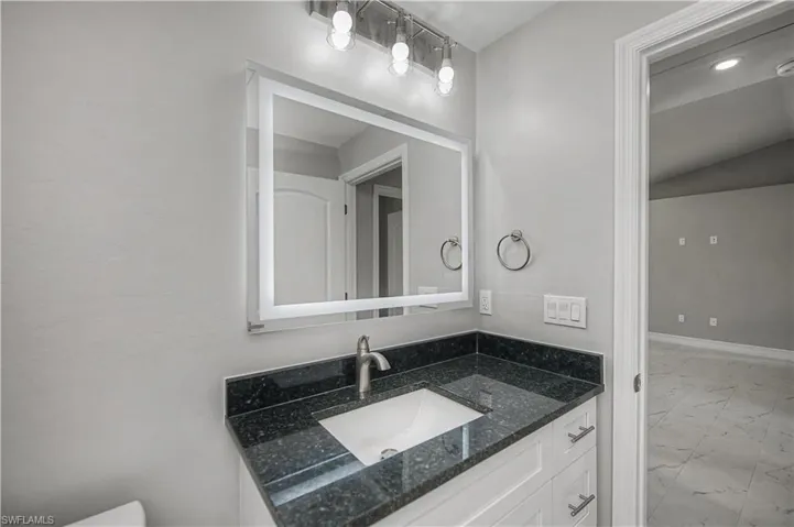 Half bath featuring vanity, light marble finish floors, and lofted ceiling