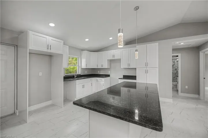 Kitchen featuring white cabinets, light marble finish floors, dark stone counters, decorative light fixtures, and vaulted ceiling