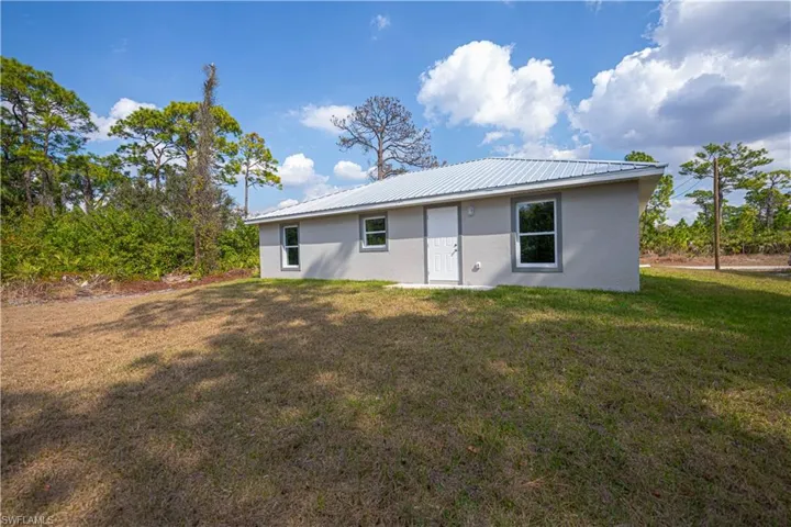Back of property with a lawn, a metal roof, and stucco siding