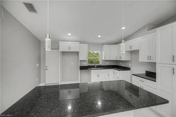 Kitchen with white cabinetry, lofted ceiling, pendant lighting, recessed lighting, and dark stone counters