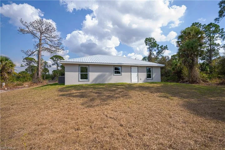 Rear view of house with a lawn, a metal roof, and stucco siding