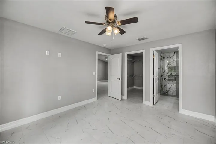 Unfurnished bedroom featuring connected bathroom, a spacious closet, light marble finish floors, and ceiling fan