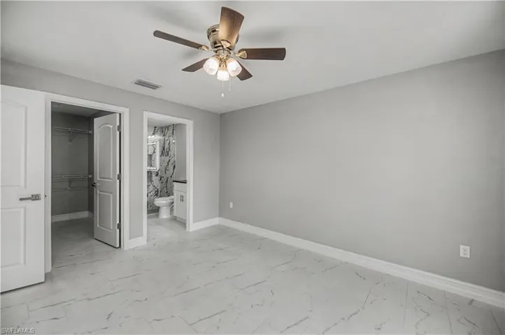 Unfurnished bedroom featuring a spacious closet, light marble finish floors, a ceiling fan, and ensuite bath