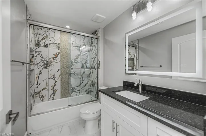 Bathroom with shower / bath combination with glass door, vanity, marble finish floors, and recessed lighting