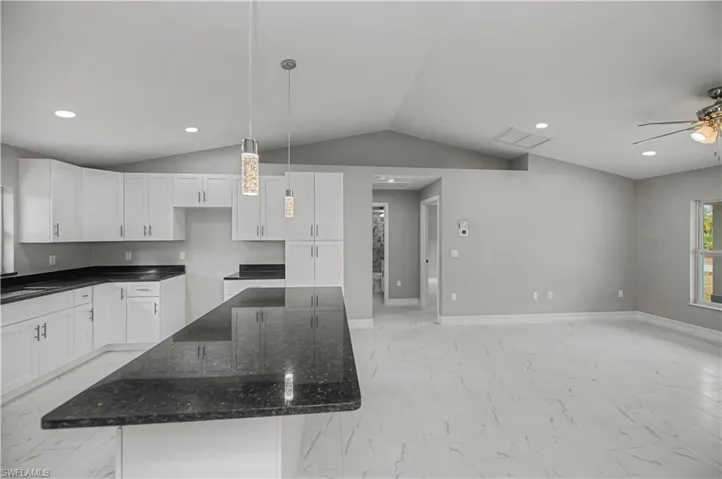 Kitchen with dark stone counters, decorative light fixtures, white cabinets, recessed lighting, and light marble finish flooring