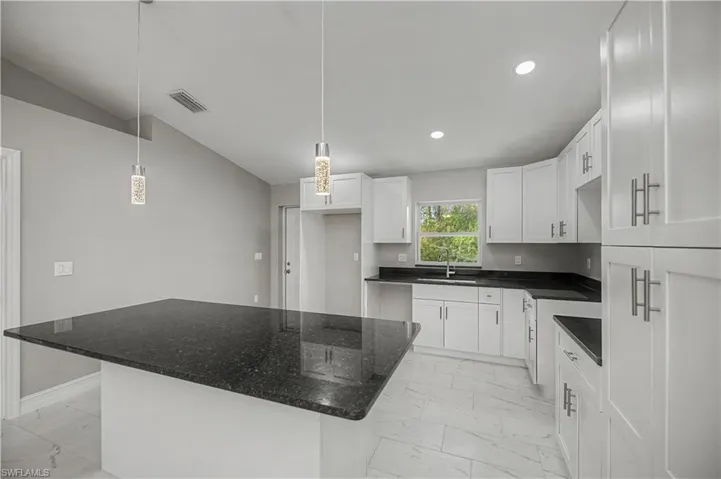 Kitchen with light marble finish flooring, white cabinetry, decorative light fixtures, a center island, and dark stone counters