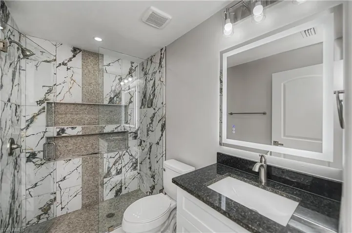 Bathroom with vanity, a marble finish shower, and recessed lighting