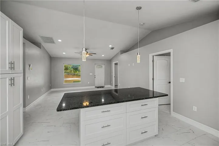 Kitchen with white cabinets, dark stone counters, open floor plan, a center island, and lofted ceiling