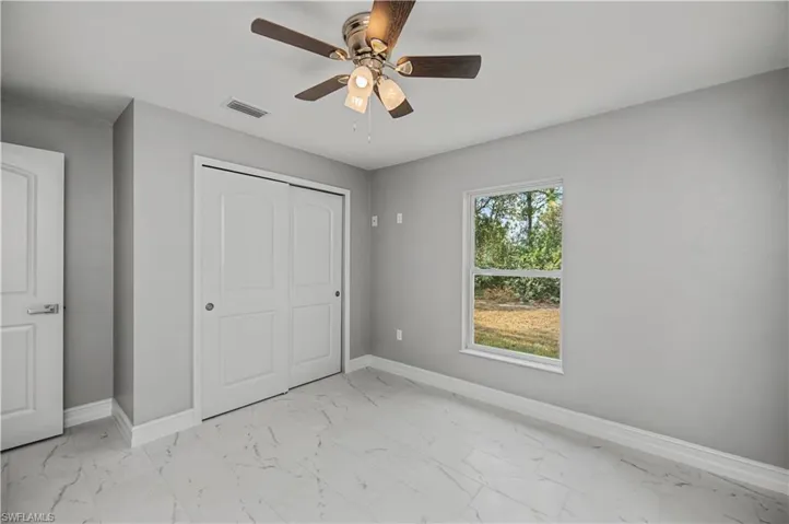 Unfurnished bedroom with a ceiling fan, light marble finish floors, and a closet