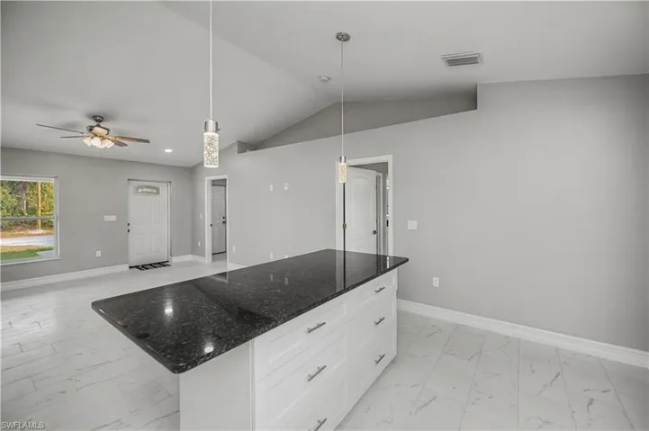 Kitchen featuring dark stone countertops, hanging light fixtures, light marble finish floors, white cabinets, and lofted ceiling