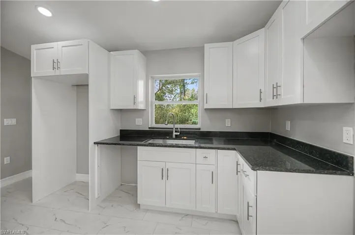 Kitchen featuring white cabinetry, light marble finish flooring, and dark stone counters