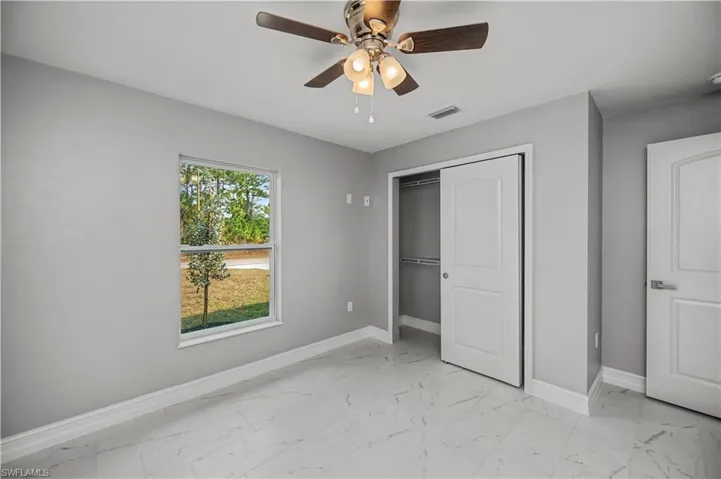 Unfurnished bedroom with light marble finish flooring, a ceiling fan, and a closet