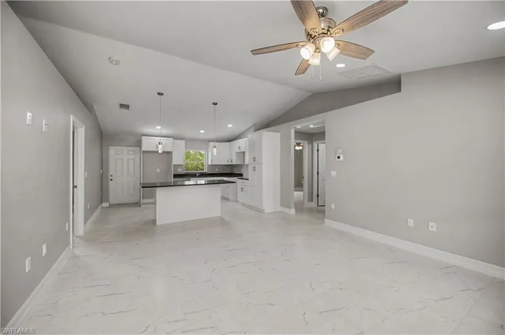 Kitchen with open floor plan, dark countertops, white cabinets, a center island, and lofted ceiling