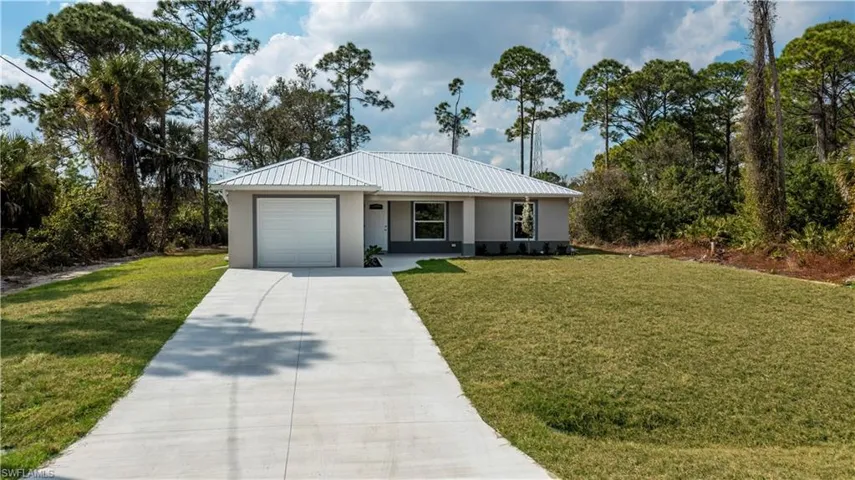 Ranch-style house with stucco siding, driveway, a front yard, a garage, and a metal roof