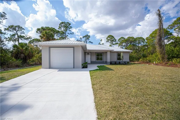 Single story home featuring a front lawn, an attached garage, driveway, stucco siding, and a metal roof