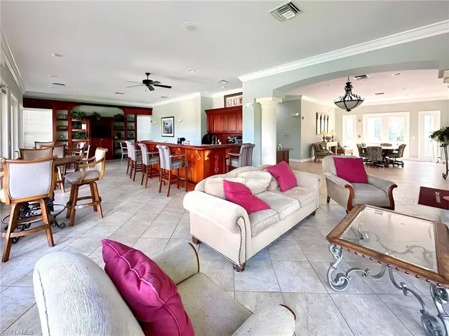 Tiled living room with decorative columns, crown molding, and ceiling fan