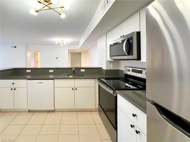 Kitchen featuring appliances with stainless steel finishes, sink, light tile patterned flooring, white cabinetry, and a notable chandelier