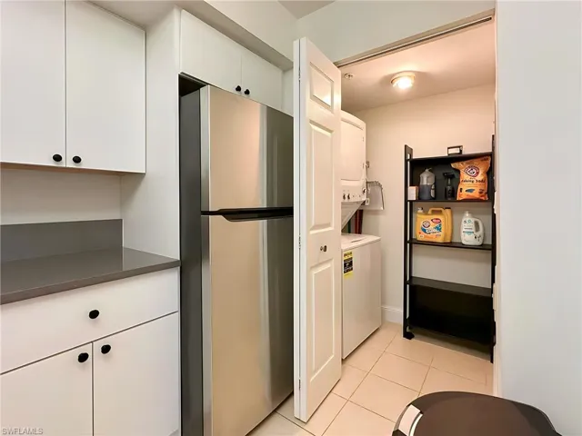 Kitchen with white cabinetry, stacked washer / drying machine, light tile patterned flooring, and stainless steel refrigerator