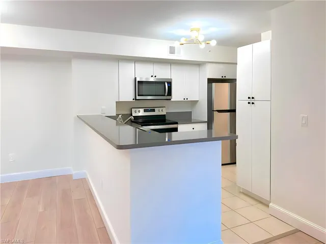 Kitchen with light hardwood / wood-style floors, kitchen peninsula, white cabinetry, and stainless steel appliances