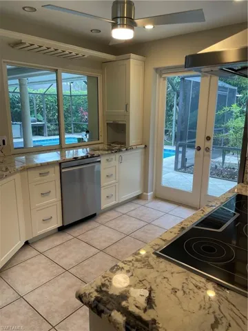 Kitchen with cooktop, white cabinetry, dishwashing machine, and light stone countertops
