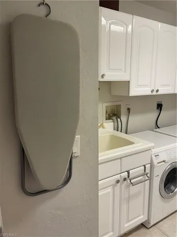 Laundry area with cabinet space, a textured wall, washer / clothes dryer, a sink, and light tile patterned flooring
