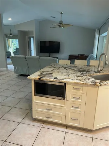 Kitchen featuring ceiling fan, light stone counters, open floor plan, white cabinetry, and a sink